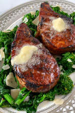 perfectly cooked pork chops with butter melting on top sitting on broccoli rabe.