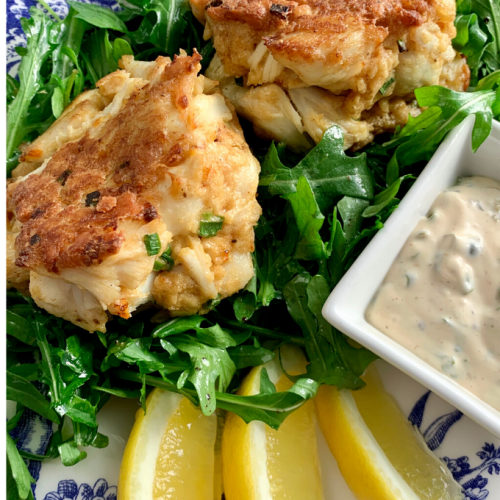 Nicely browned jumbo lump Crab Cakes with a Lemon Caper Sauce on a plate with 3 lemon wedges