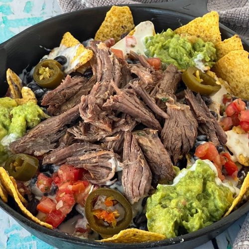a picture of a cast iron skillet filled with loaded beer-braised beef short rib nachos with many toppings