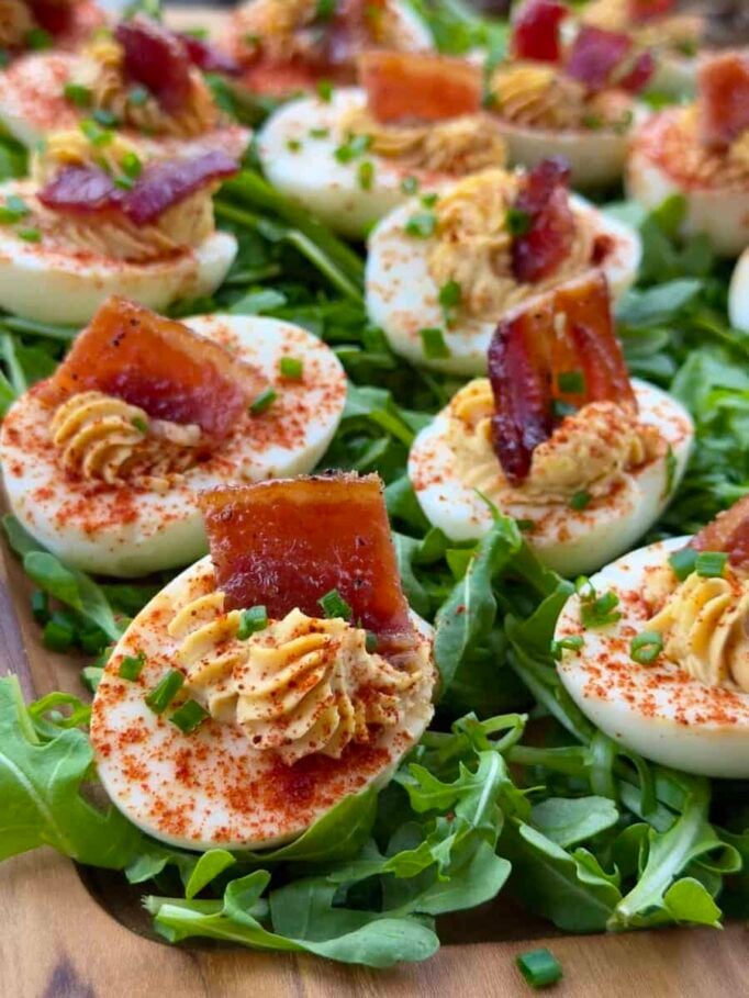 A serving platter of many BBQ deviled eggs with candied bacon on top