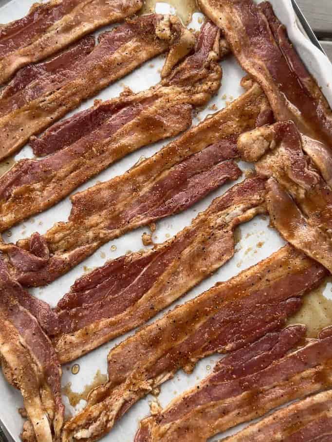 a tray of raw, thick cut bacon that has been covered lightly with brown sugar and BBQ rub to make candied bacon.