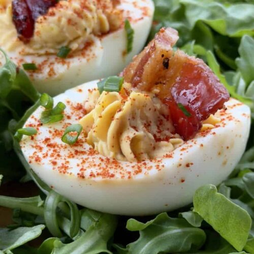 BBQ deviled eggs with candied bacon on a serving platter with arugula