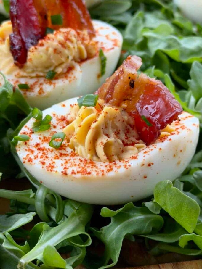 BBQ deviled eggs with candied bacon on a serving platter with arugula